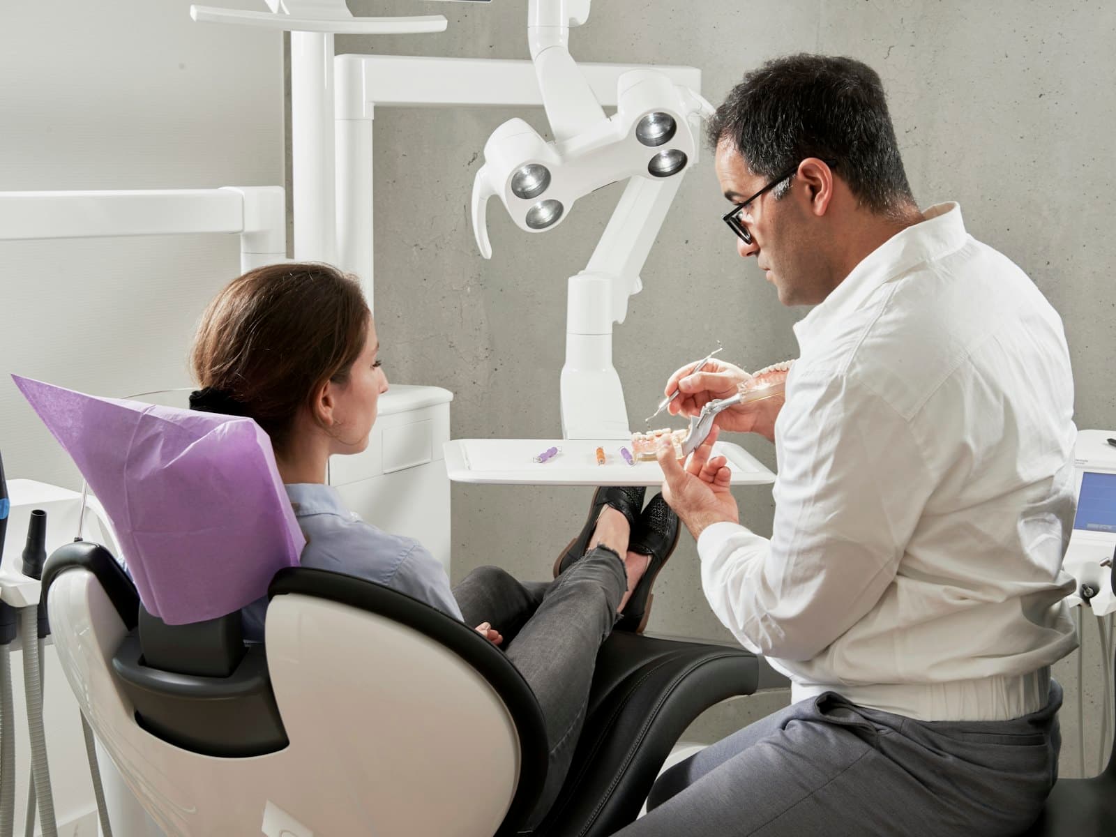 Nha sĩ ngồi cạnh ghế khám, dùng mô hình hàm để giải thích cho khách